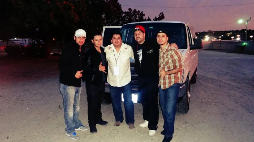 Cinco hombres posan frente a una van blanca al atardecer