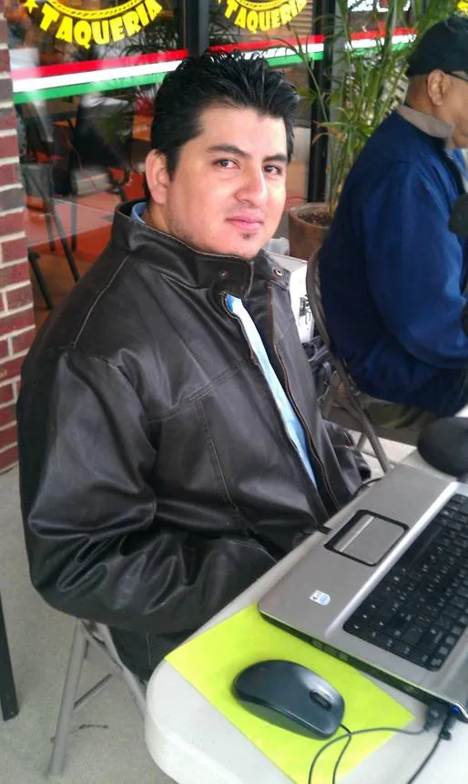 Hombre con chamarra negra sentado frente a una laptop en un evento de radio