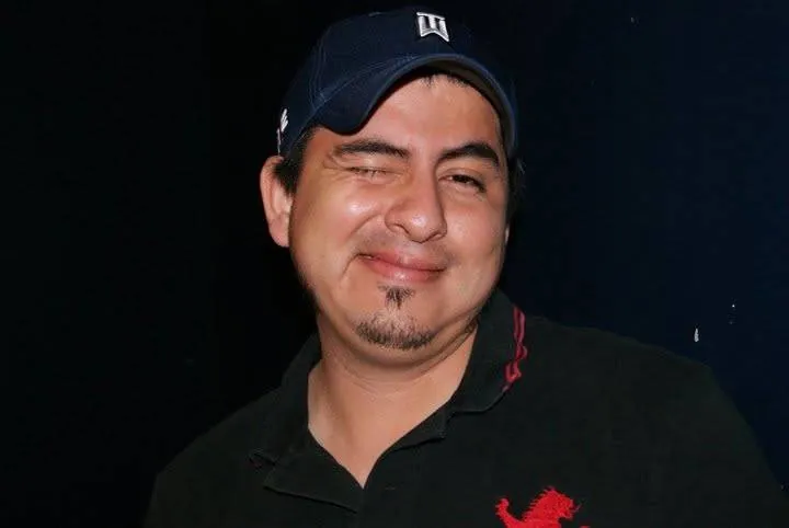Retrato de un hombre con gorra azul marino guiñando un ojo sobre fondo oscuro
