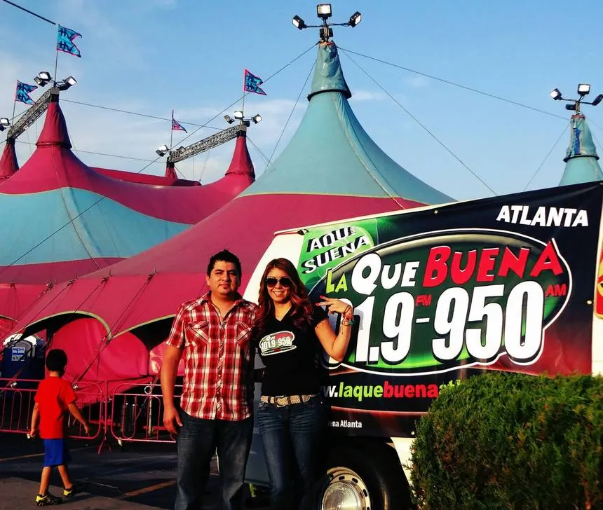Dos personas frente a la unidad móvil de La Que Buena en Atlanta, junto a una carpa de circo